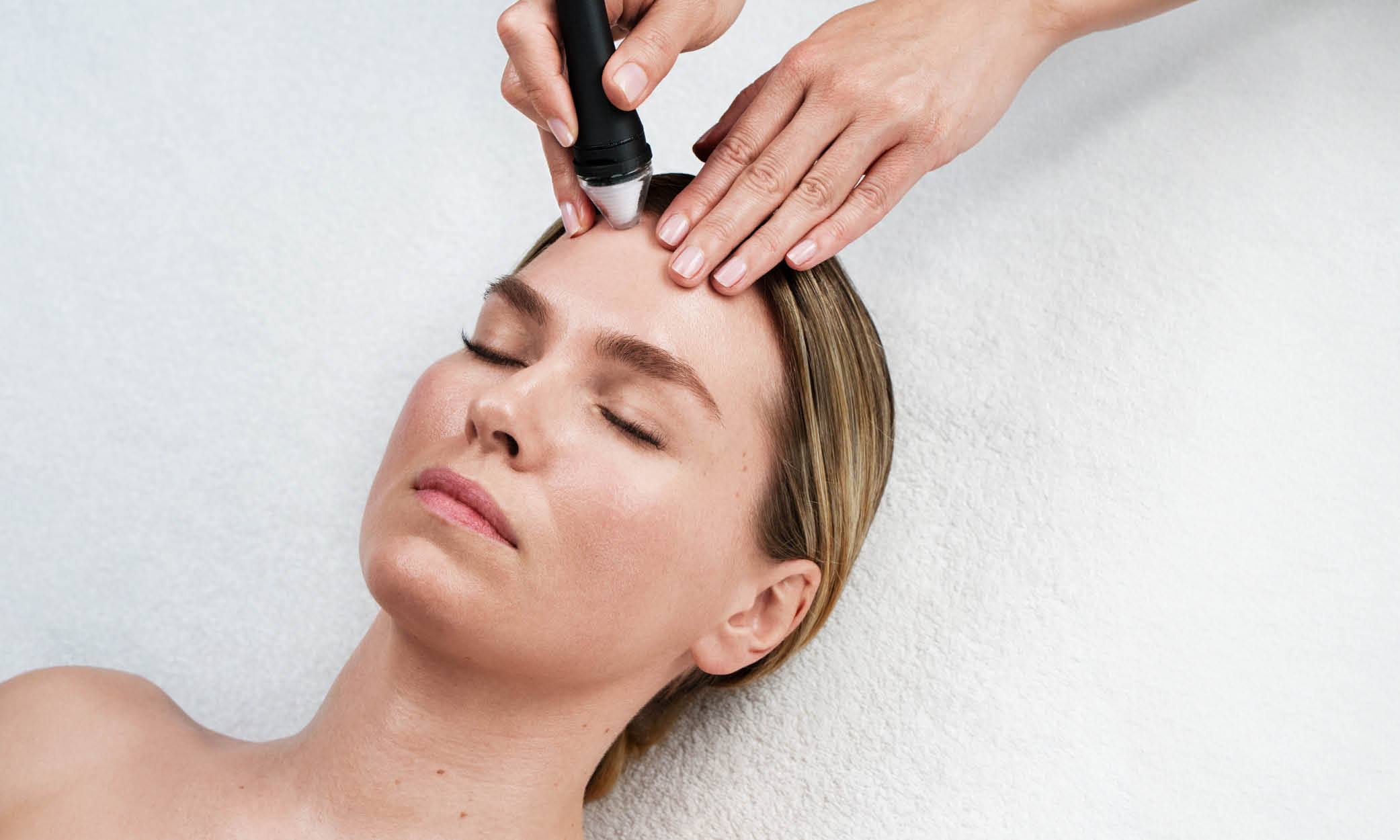 Frau mit geschlossenen Augen, liegend bei einer Gesichtsbehandlung mit Apparat.