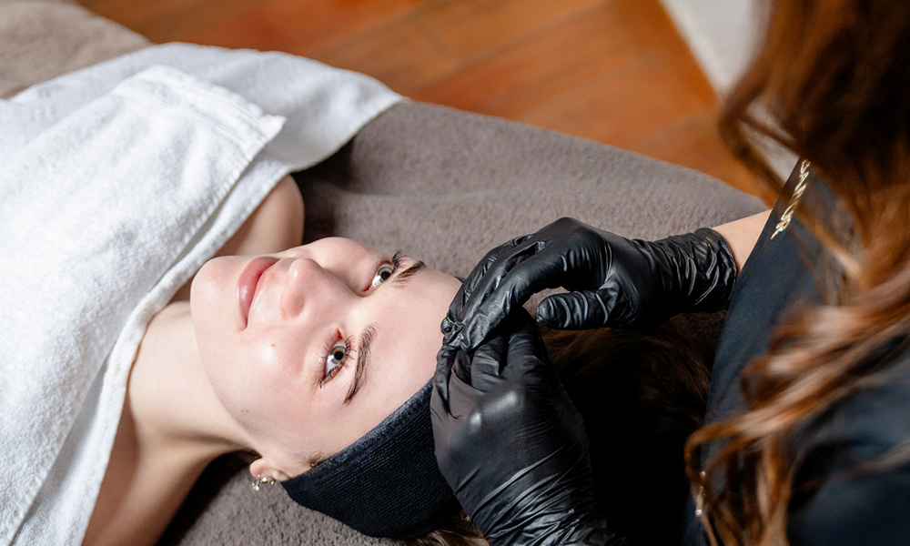 Kosmetikbehandlung: Kundin liegt, Kosmetikerin arbeitet an der Stirn.