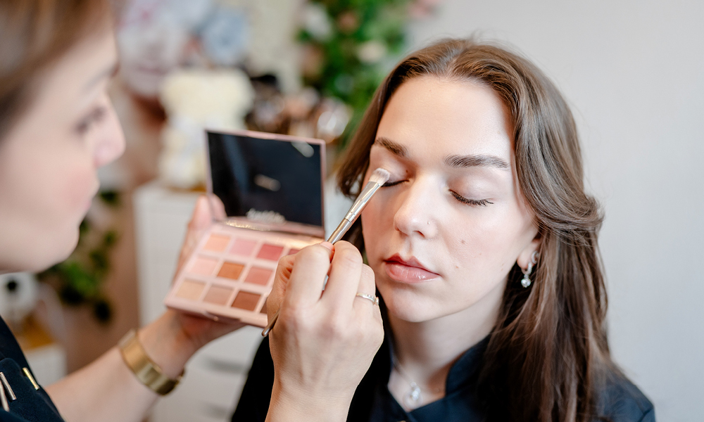 Kosmetikerin trägt Make-up mit Pinsel bei einer Kundin auf.
