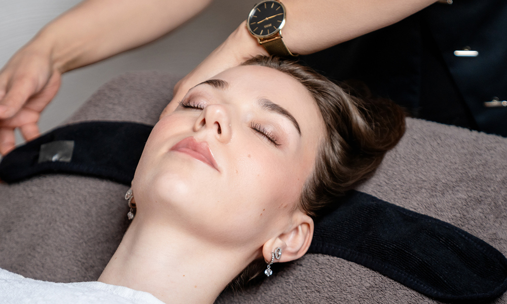 Kosmetikbehandlung: Kundin liegt entspannt, Kosmetikerin arbeitet am Kopfbereich.