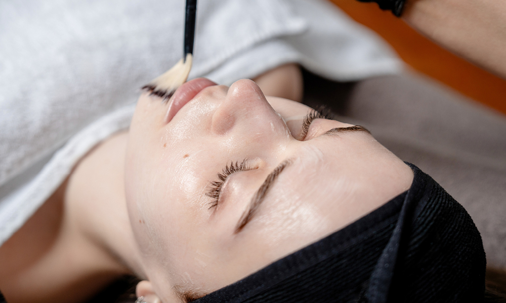 Kosmetikerin behandelt Kundin und trägt Produkt im Gesicht mit einem Pinsel auf.