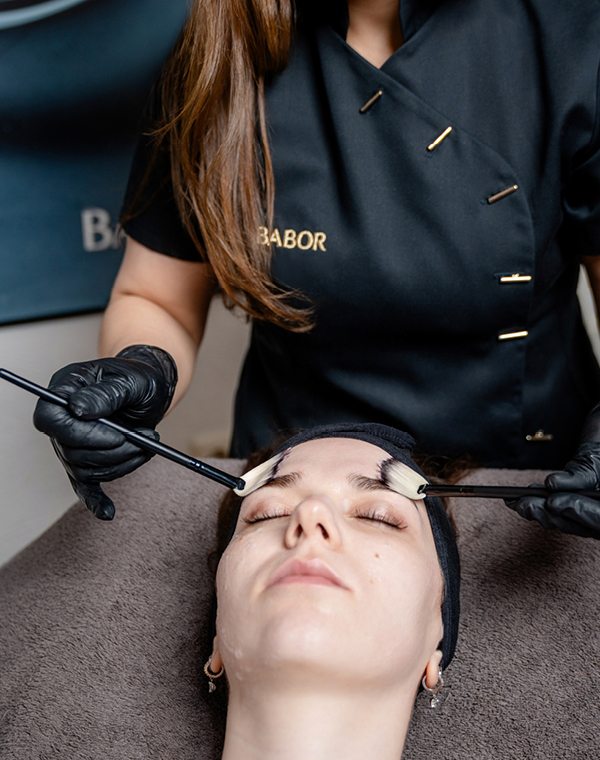 Kosmetikerin behandelt Kundin und trägt Produkt im Gesicht mit einem Pinsel auf.