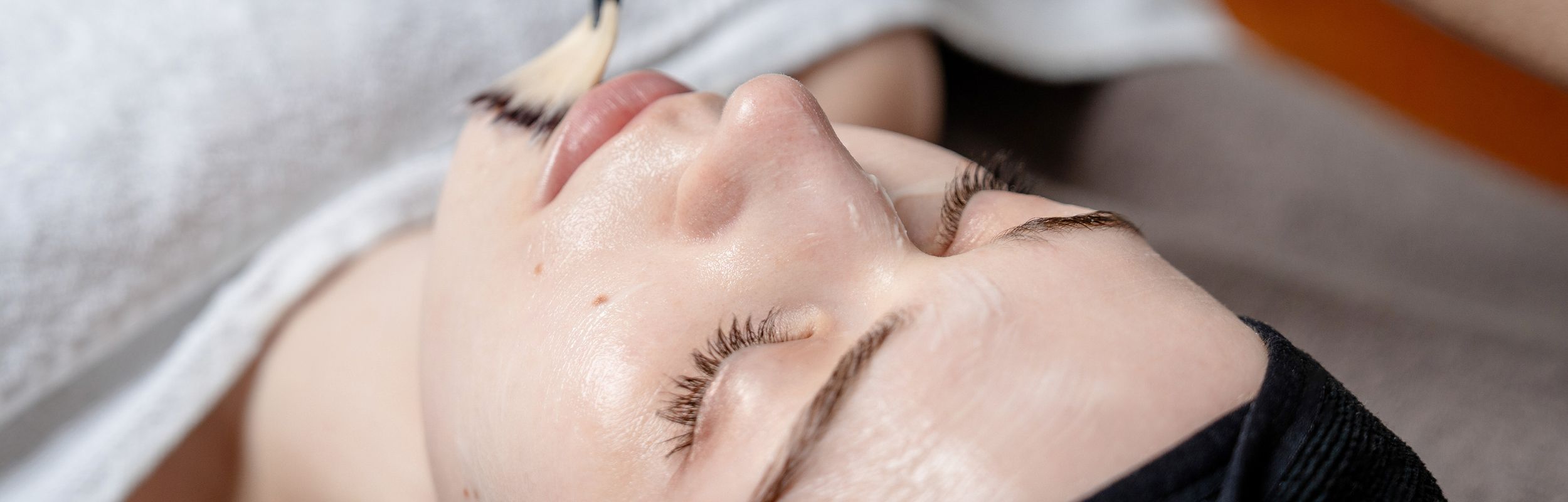 Kosmetikerin behandelt Kundin und trägt Produkt im Gesicht mit einem Pinsel auf.
