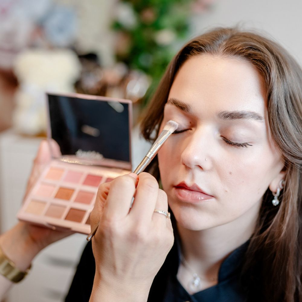 Kosmetikerin trägt Make-up mit Pinsel bei einer Kundin auf.