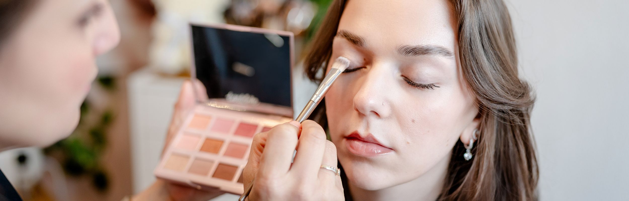 Kosmetikerin trägt Make-up mit Pinsel bei einer Kundin auf.